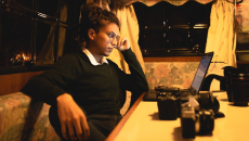 A person at a corner table holds their head as they look at their laptop,