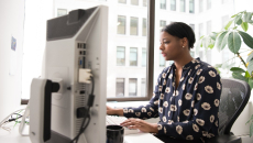 A female patient navigator sits at her desk working on a desktop.