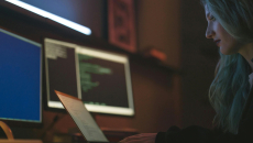 A security IT professional with long hair sits at a desk and monitors a client system remotely
