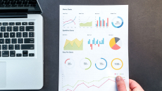 A section of a laptop appears next to print outs of health research data analytics.