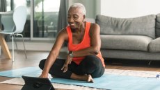 Woman sits on yoga mat in living room looking through data on her tablet