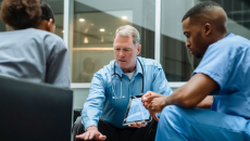 Doctor with tablet talking to seated coworkers