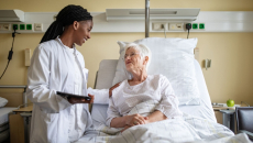 A doctor holding a digital tablet interacting with a senior patient in bed.