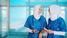 Nurses wearing hijabs conversing while holding their smartphones