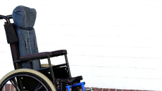 A wheelchair, perhaps for an ALS patient, sits vacant by a wall.