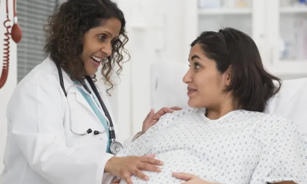 Doctor talking to pregnant patient and placing had on stomach