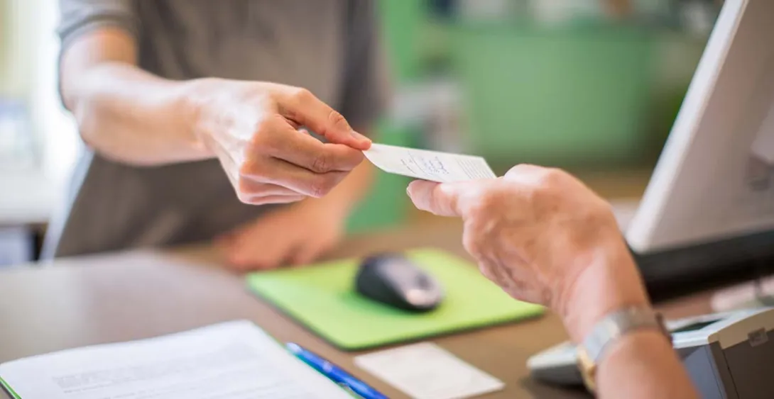 Person behind a desk handing a slip of paper to another