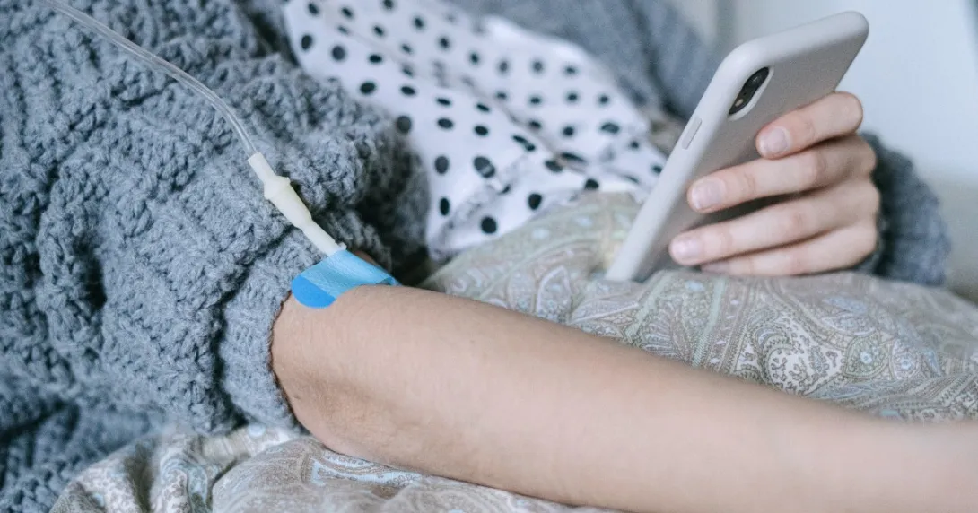 A patient looking at phone while connected to an IV