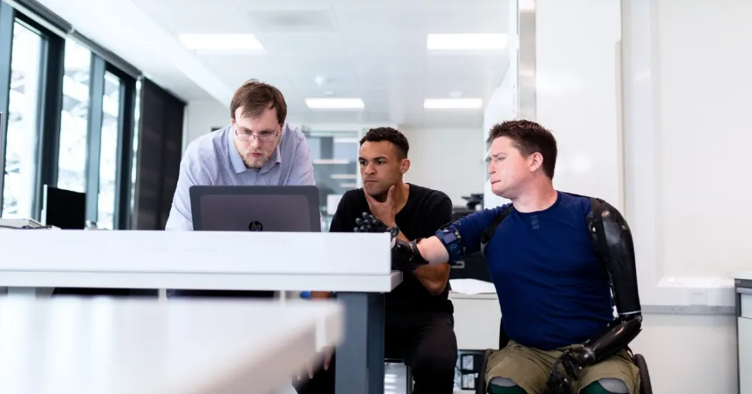 Three people in an office sit looking at a computer