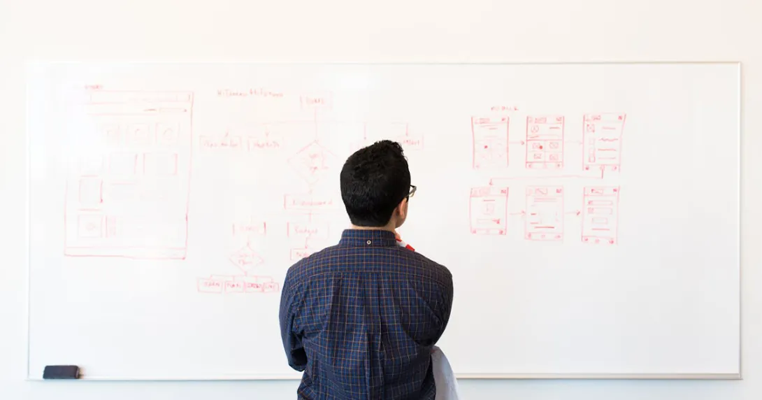 Developer faces a whiteboard looking at a tech stack diagram