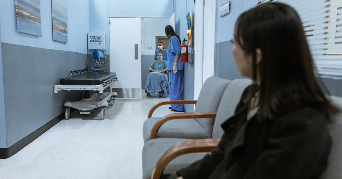 Adult sits as child is wheeled out of a medical test.
