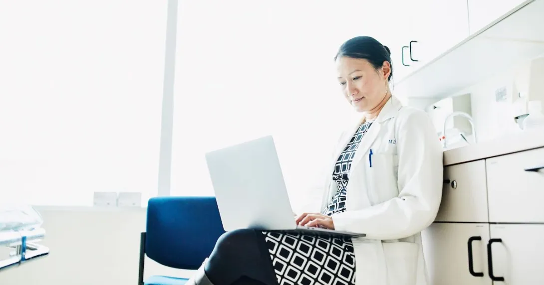 Clinician works on her laptop in a patient room.