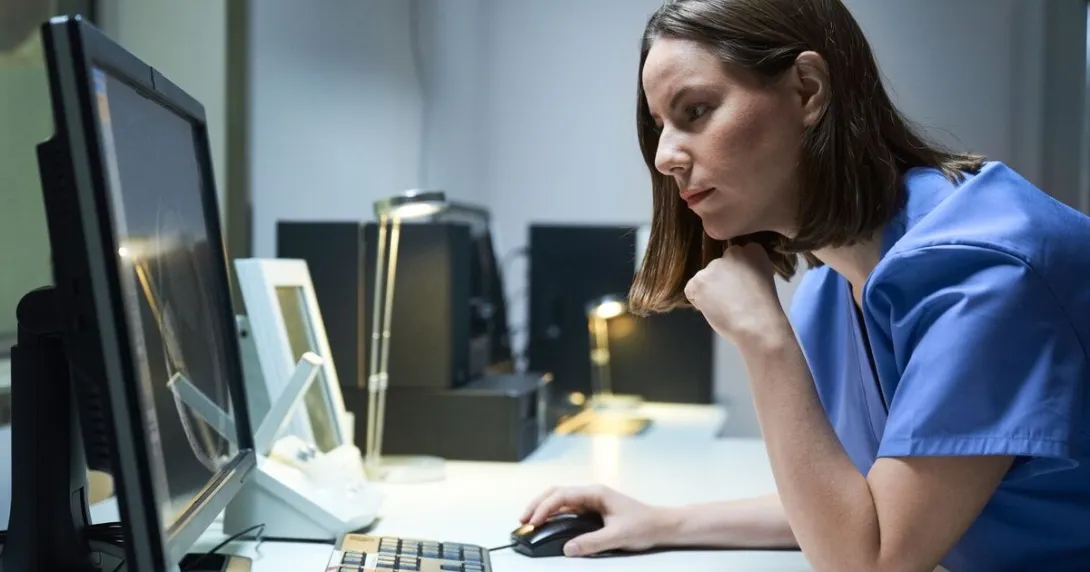 Clinician in blue scrubs looks at a computer monitor