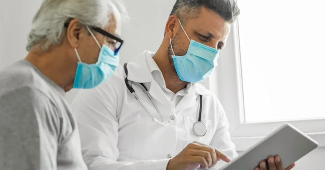 Doctor and patient wearing masks look at a tablet in an exam room