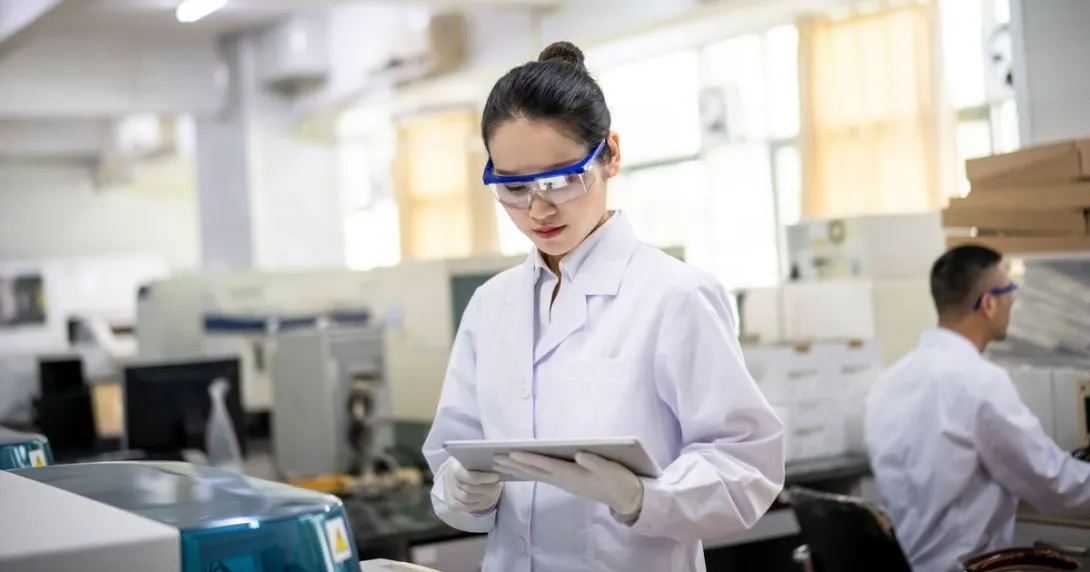 A scientist in a lab gown holding a digital tablet