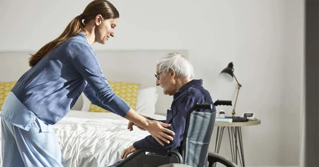 Nurse helps an elderly patient into a wheelchair at home