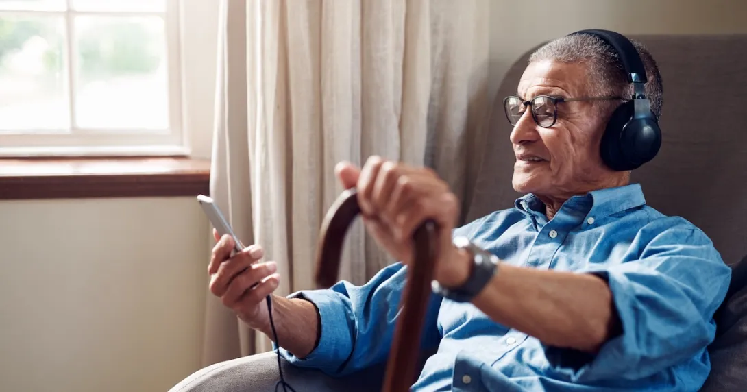 An elderly person using a smartphone and headphones sitting on a chair