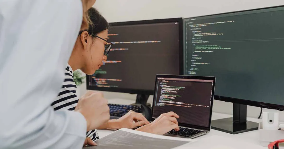 Workers coding on a laptop with dual monitors