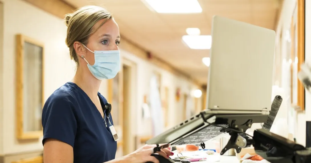 A nurse checking on a patient's record on a hallway desktop computer