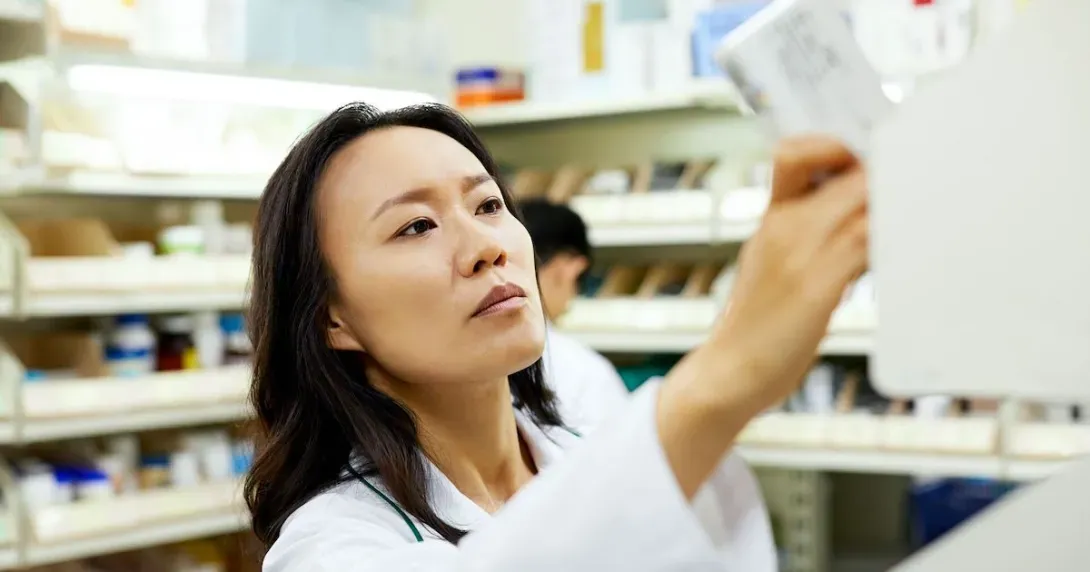Pharmacist takes a prescription from a shelf and reads it  