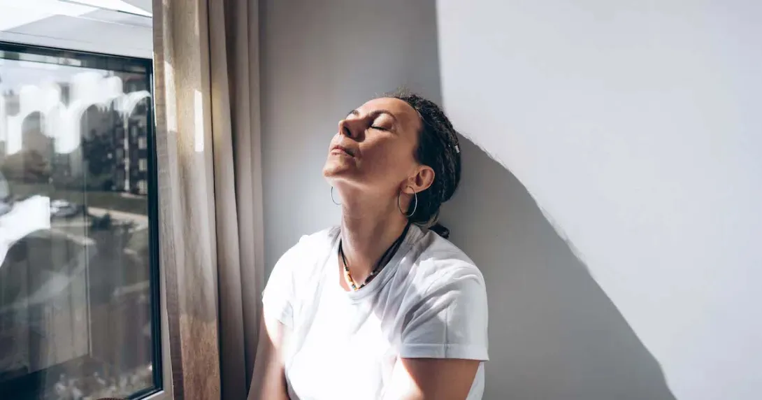 Stressed woman sits with her head against a wall 