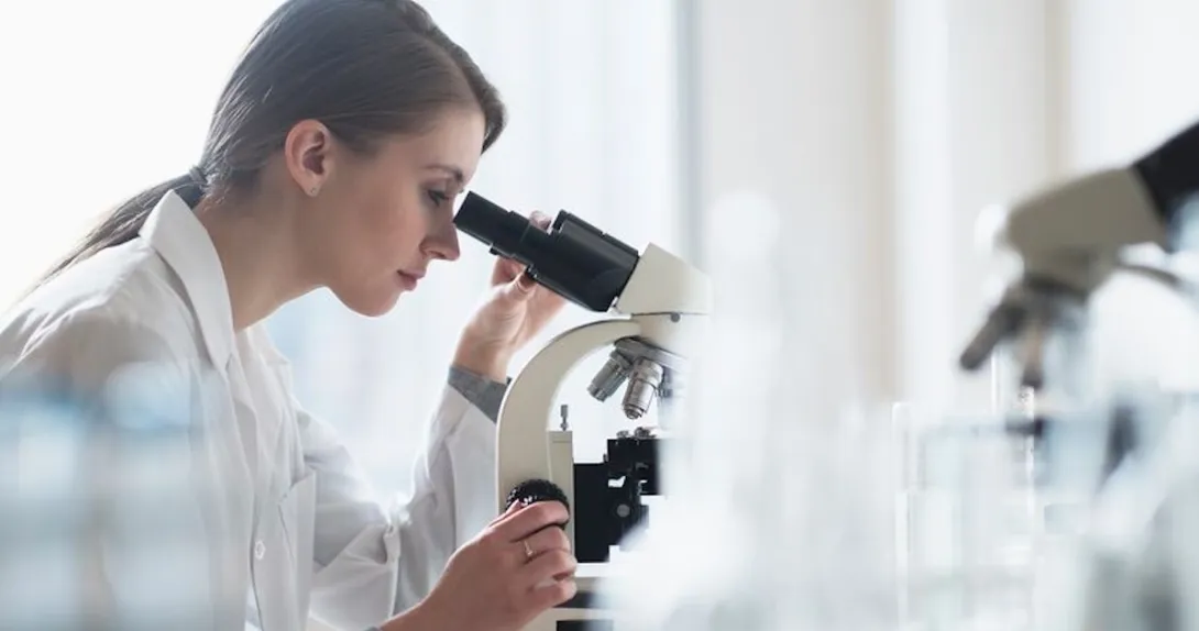 Healthcare worker looking through microscope in lab