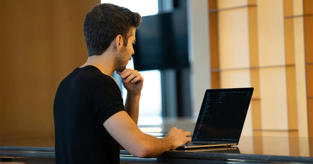 Man in black tshirt codes on a laptop