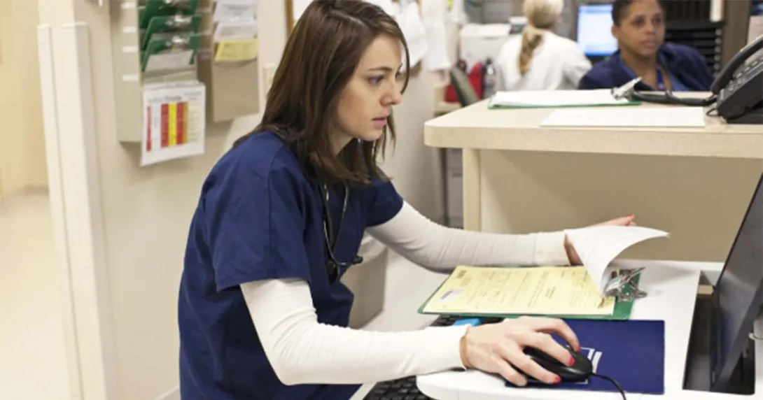 Nurse in scrubs sitting at a computer with notes