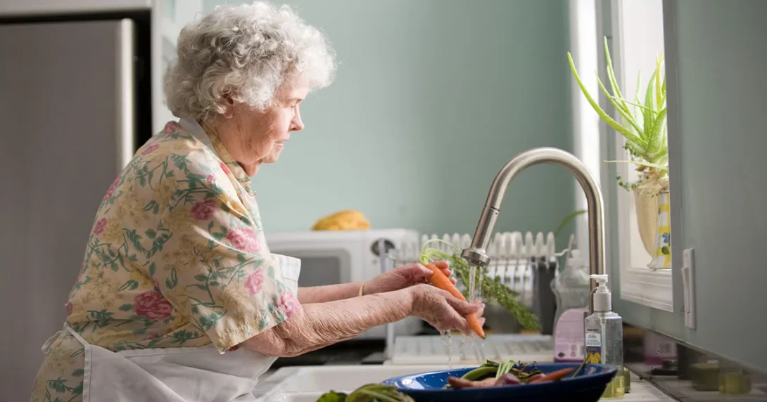 Woman with short hair washes carrots with an electric faucet.
