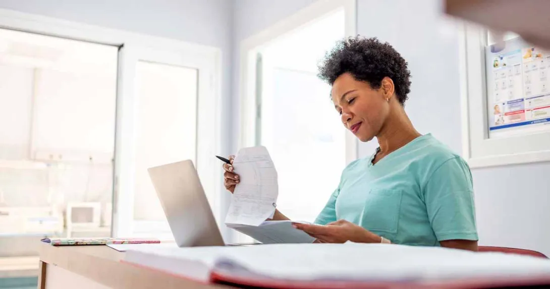 Healthcare worker looking at papers at a desk with a laptop