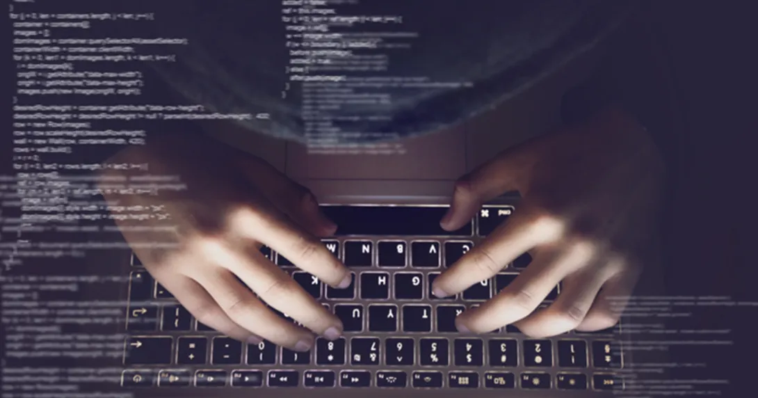 Code appears in the foreground over hands on a laptop.