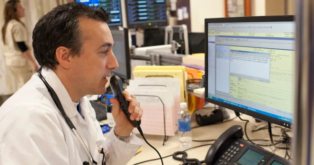 Doctor sits at a desktop and dictates notes into an EHR