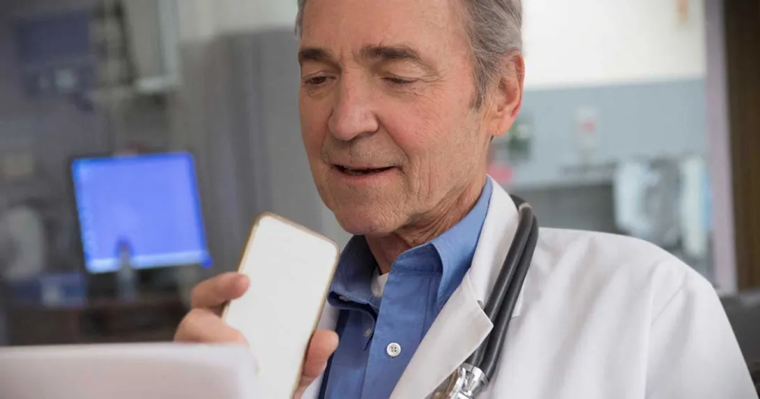Gray-haired doctor sitting at a monitor and talking into a cell phone