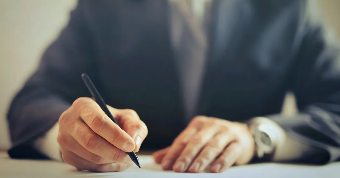 The hands of an executive in a suit are signing a document with a pen.