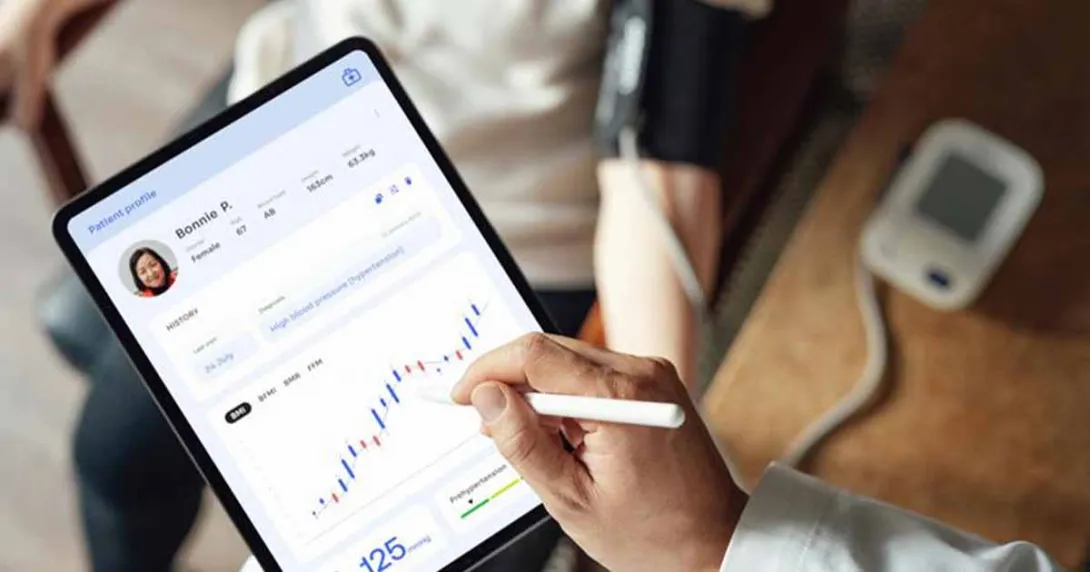 Healthcare worker looking at medical record on tablet with patient in background