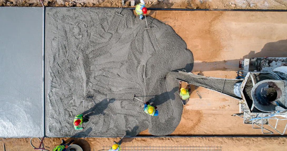 Workers lay out a layer of cement on a foundation.