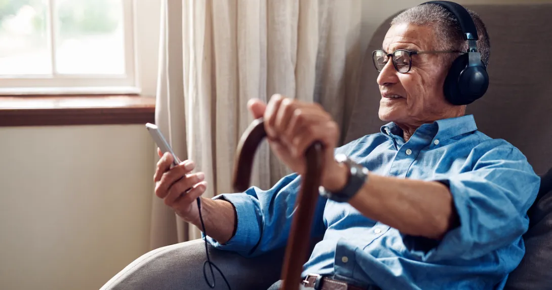 Person with cane and smartphone sitting with headphones on