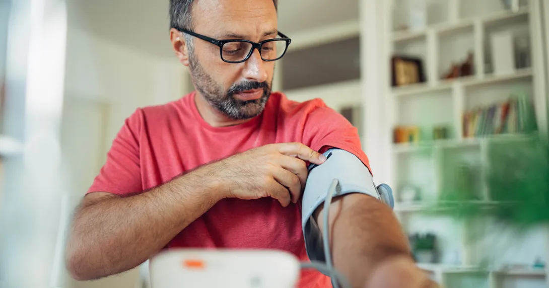 Man in a red tshirt measures his blood pressure with an RPM device.