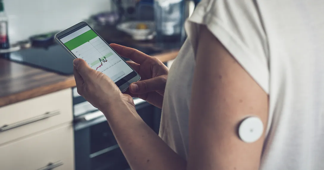 Person wearing blood glucose monitor using smartphone app