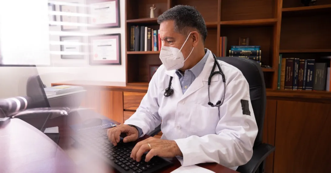 Male doctor in a medical mask works at his desktop.