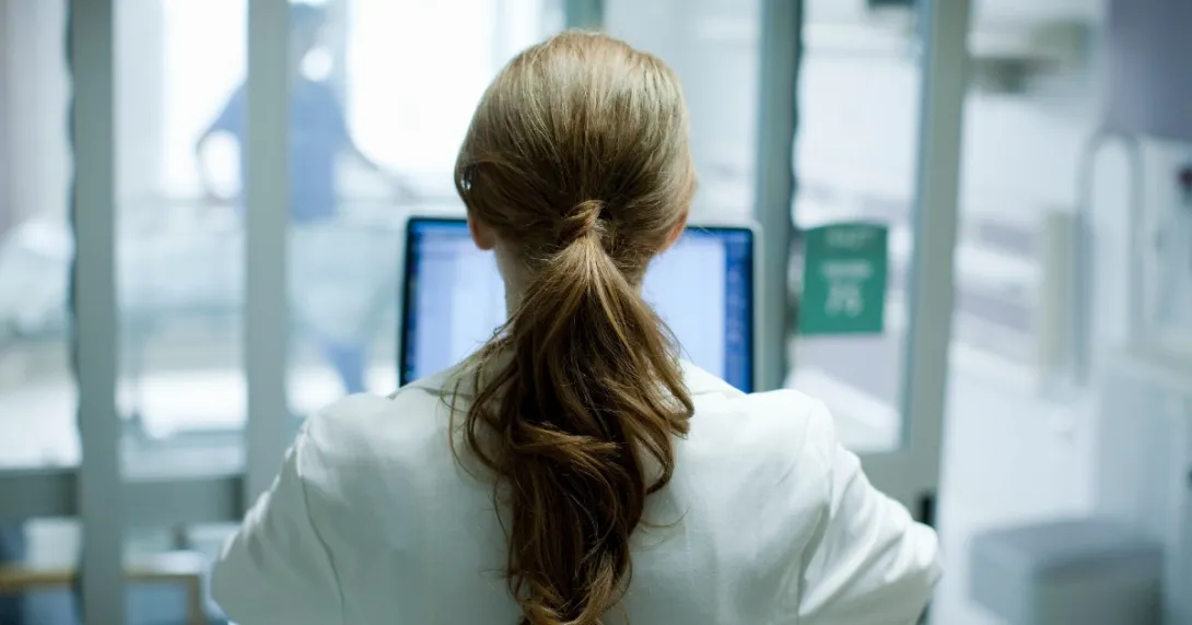Doctor with long hair in a ponytail sits and works on a laptop