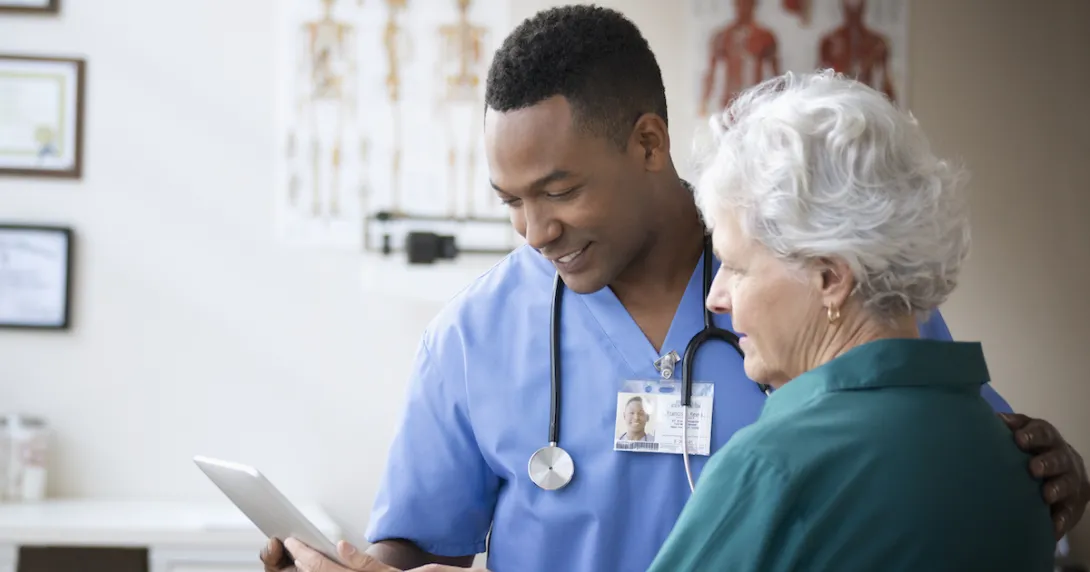 Doctor and patient look at a tablet while conversing.