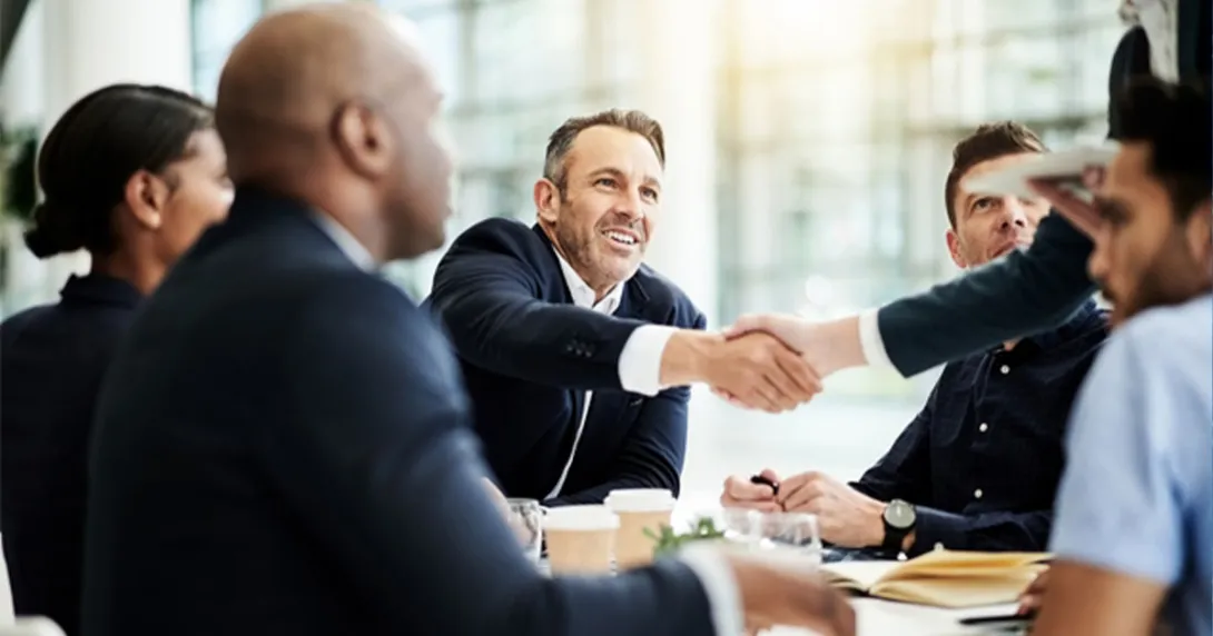 Two people shake hands in a meeting at a table