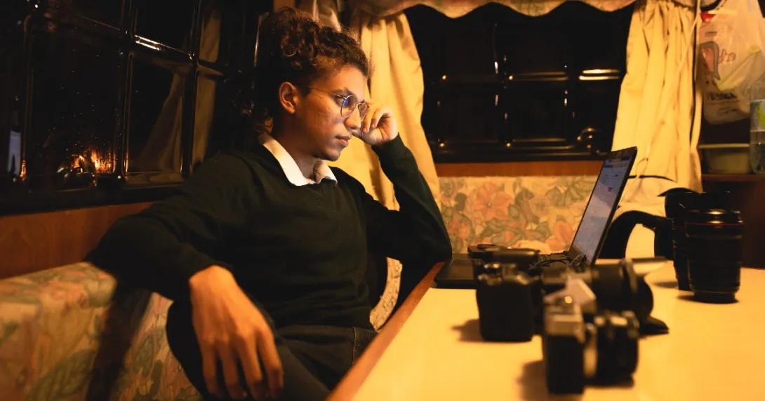 A person at a corner table holds their head as they look at their laptop,