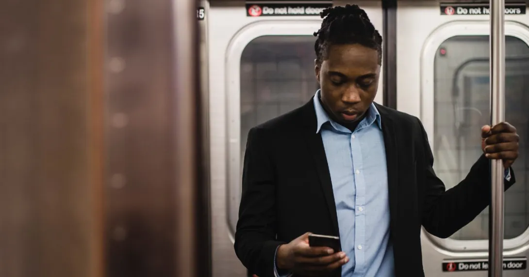 A person in a suit jacket looks down at his cellphone while standing and riding the subway.