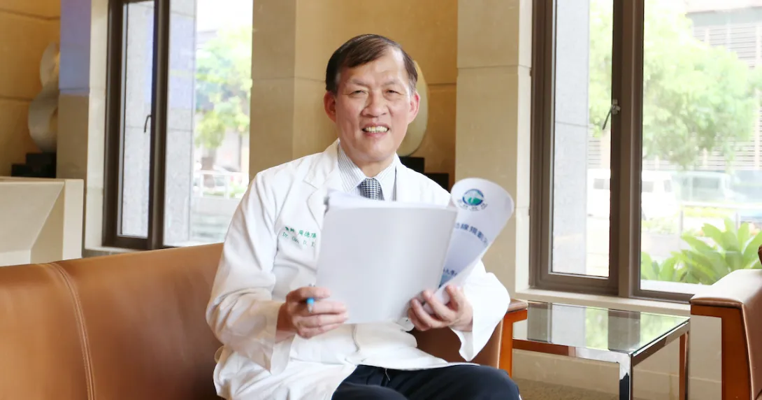 China Medical University Hospital Superintendent Dr Der-Yang Cho sitting on a chair while holding a paper report