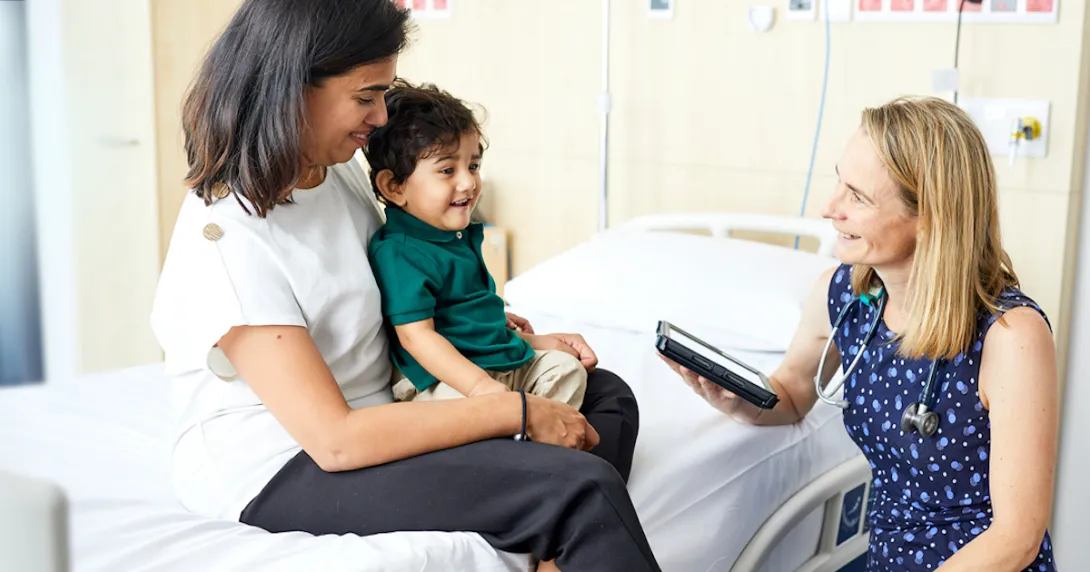 A doctor holding a digital tablet is sitting beside a mother and her child