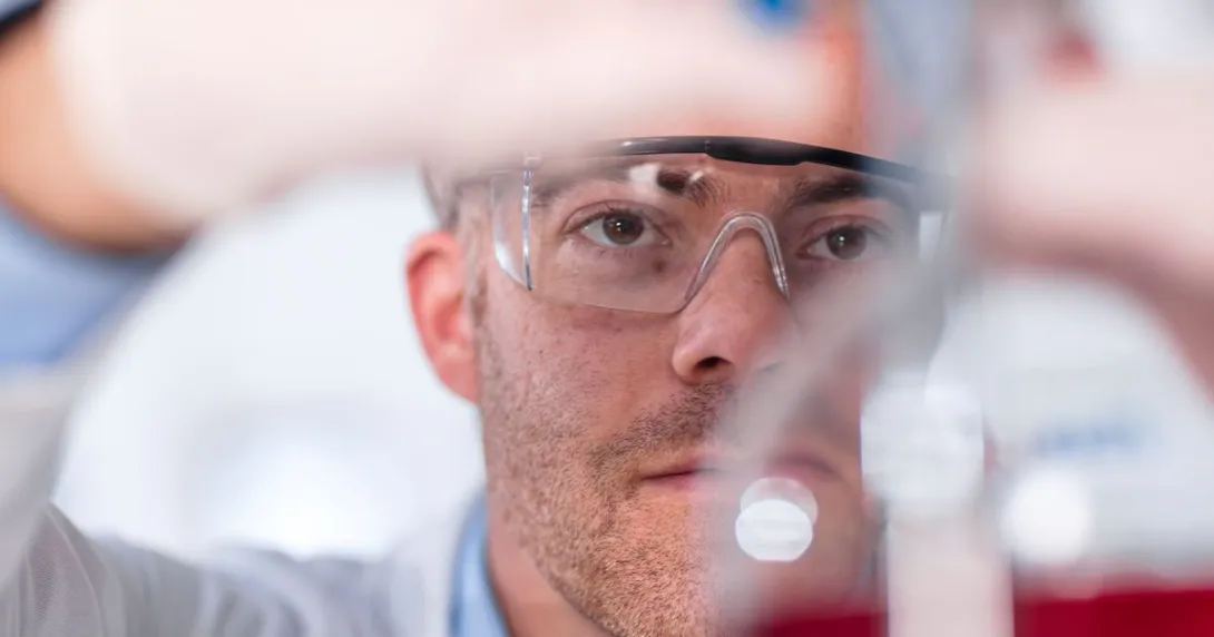 Lab worker with safety glasses looking into a beaker