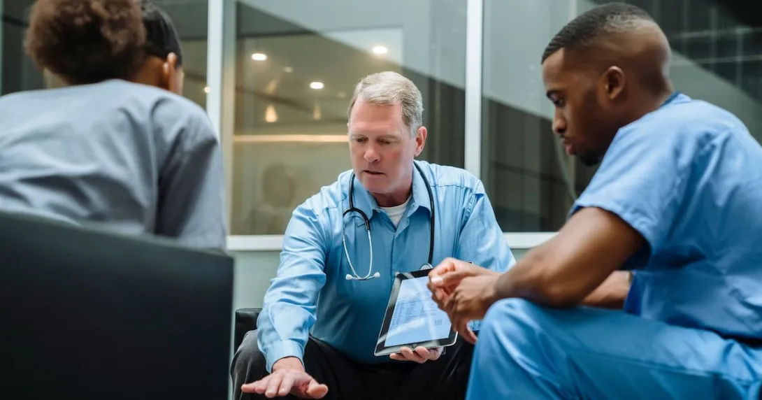 Doctor with tablet talking to seated coworkers