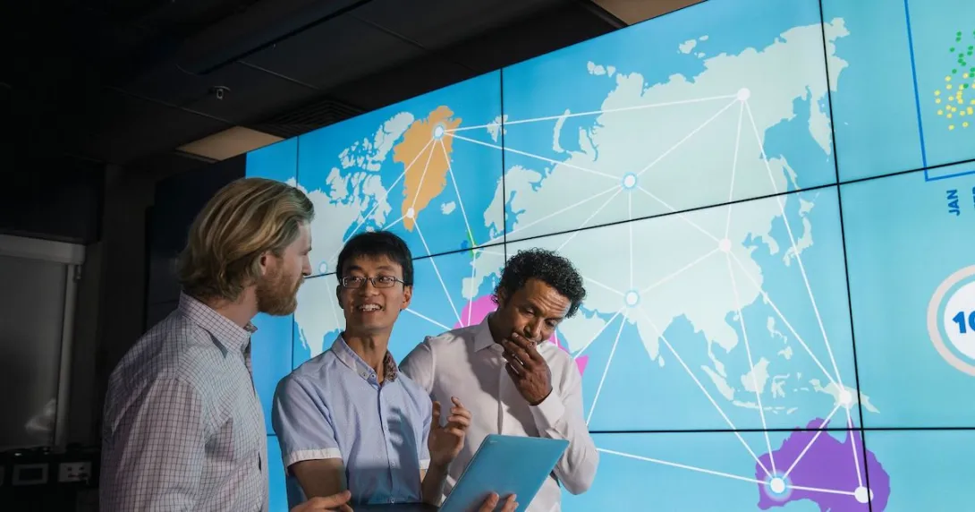 Workers looking at a tablet with world map projected in background